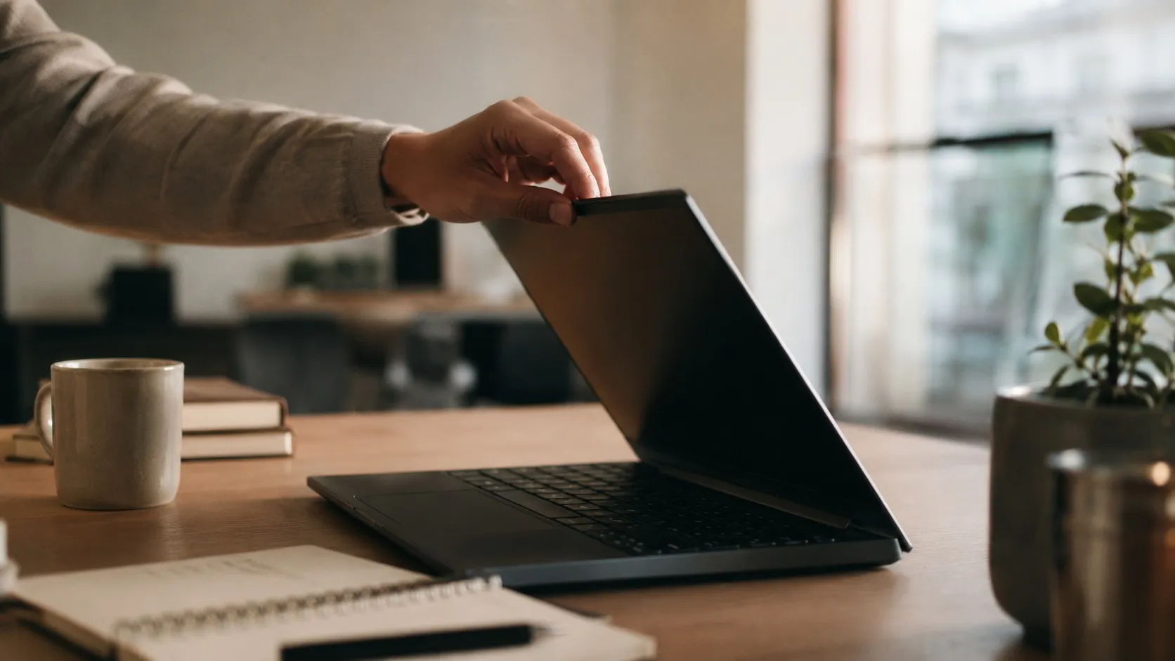 En hand öppnar locket på en laptop på ett skrivbord